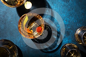 Old fashioned alcoholic cocktail with bourbon whiskey, marascino cherry and orange peel garnish, blue table, copy space, top view