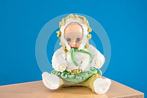 Old Fashioned baby Doll dressed in knitted costume sits on shelf on blue background