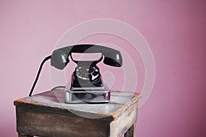 Old-fashioned black telephone on pink background