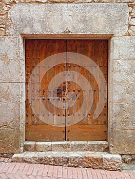 Old-fashioned brown wooden outside door with two metal knockers and a lock in an old stone wall. Architecture and medieval