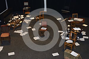 Old-fashioned chairs, chests and pieces of paper put in a mess on a theatre stage