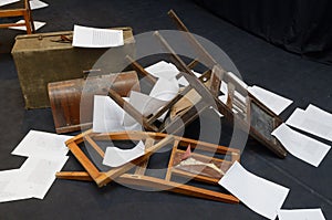 Old-fashioned chairs, chests and pieces of paper put in a mess on a theatre stage