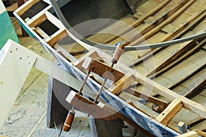 Old fashioned clamp holding curved wood being used to build a wooden boat