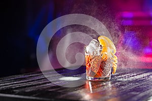 Old fashioned classic cocktail in crystal glass with ice and orange on the table on nightclub background