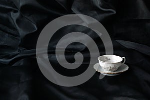 Old fashioned classic and vintage cup of tea or coffee on black satin background