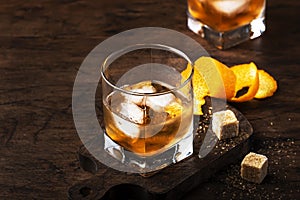 Old fashioned cocktail with bourbon, cane sugar, orange slice, cherry and orange peel garnish, vintage wood table, copy space