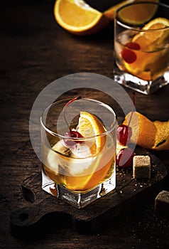 Old fashioned cocktail with bourbon, cane sugar, orange slice, cherry and orange peel garnish, vintage wood table, copy space