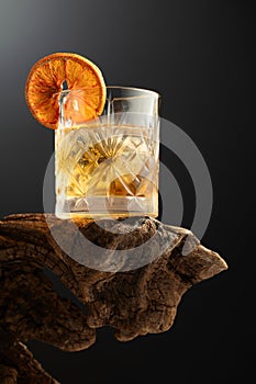 Old fashioned cocktail with ice and dried orange slice on a old snag