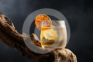 Old fashioned cocktail with ice and dried orange slice on a old snag