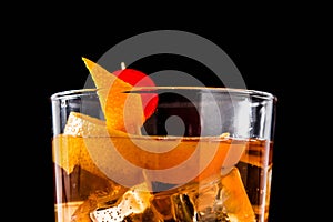 Old fashioned cocktail with orange and cherry on black background.
