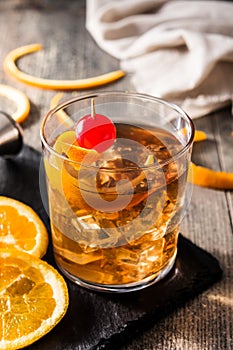 Old fashioned cocktail with orange and cherry on wood
