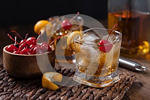 Old fashioned cocktail with orange peel and cherry