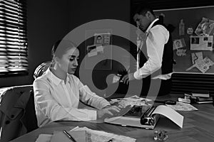 Old fashioned detective and her colleague working in office. Black and white effect