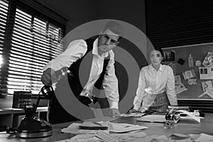 Old fashioned detective and his colleague working in office. Black and white effect