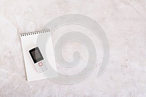 Old-fashioned feature telephone on a notepad on a gray background top view