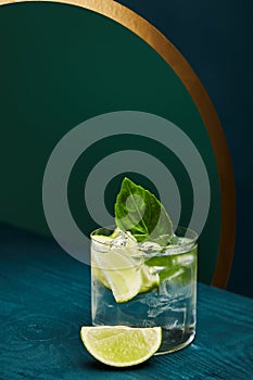 Old fashioned glass with fresh drink, mint leaf and lime slice on blue wooden surface