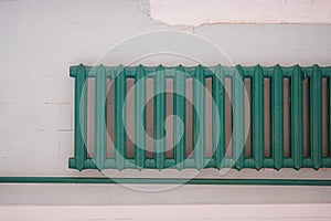 Old-fashioned green heating radiator on a grey tile wall. Indoor heating system