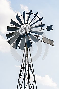 Old-fashioned metal wind pump against pale blue sky with white clouds