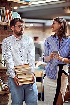 Old-fashioned nerd carrying pile of books at library watching young female with cell phone in her hands. books vs e-books concept