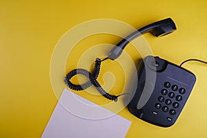 Old fashioned phone on yellow background with blank paper and pen
