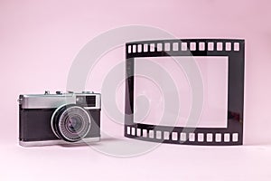 Old fashioned photography camera and photo frame in shape of film tape roll on plain pink background