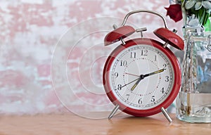 Old fashioned red alarm clock sitting on a table with rose colored background