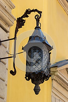 Old-fashioned street wall lamp made of black metal. Gray facade of an old house with a window and a wooden frame. Lviv, Ukraine