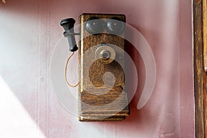 Old fashioned telephone earphone from the 1900s, on a wall. Pink background