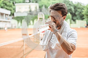 old-fashioned tennis player with towel drinking water after training