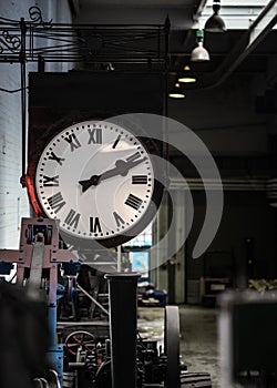 Old fashioned vintage big industry factory clock hanging with roman numerals in abandoned building no workers.