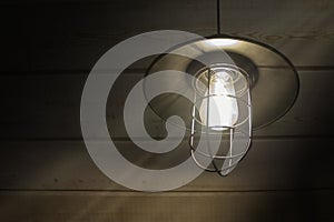 Old fashioned vintage lantern lamp burning with a soft glow light in an antique rustic country barn with aged wood wall
