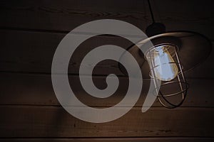 Old fashioned vintage lantern lamp burning with a soft glow light in an antique rustic country barn with aged wood wall and