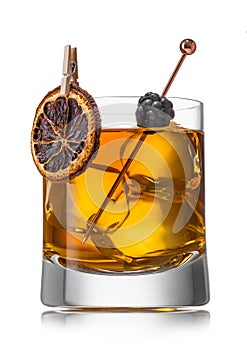 Old fashioned whiskey cocktail with dry orange and blackberry and large ice cubes on white background