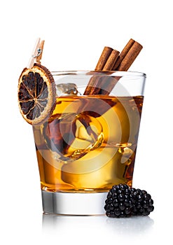 Old fashioned whiskey cocktail with dry orange,cinnamon and blackberries and large ice cubes on white background