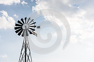 Old-fashioned wind powered water pump against pale blue sky with clouds