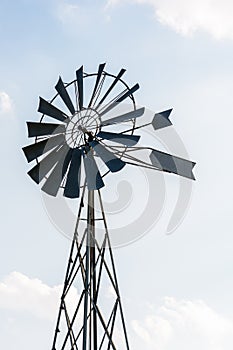 Old-fashioned wind powered water pump against pale blue sky with white clouds
