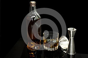 Old fashon glass alcohol Scotch whiskey and stones to cool golden drink next to funnel and measuring cup