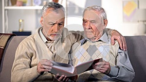 Old father and son watching family album on sofa at home, togetherness, close-up