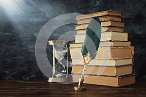 Old feather quill ink pen with inkwell and old books over wooden desk in front of black wall background. Conceptual photo on