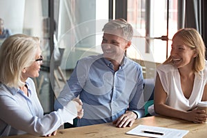 Old female broker handshake happy young couple clients make deal