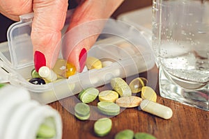 Old female fingers with manicure take omega 3 capsule from the container with mix of vitamins and supplements.