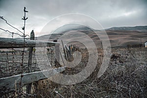 Old fence in a field at dawn. Dawn in autumn field. Hills in morning haze. Grass covered with autumn hoarfrost. Nature in