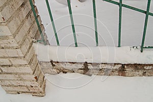 Old fence with metal bars and brick posts, cracked plaster due to adverse weather conditions, outdoors, snow, winter, cold