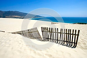 Old fence sticking out of deserted sandy beach dunes