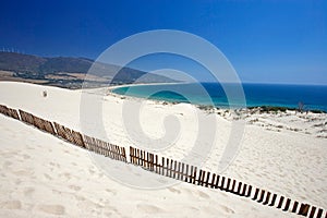 Old fence sticking out of deserted sandy beach dunes