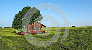 Old Fendt tractor with trailed rotary tedder. Hay ready to be harvested. Wood storage in the countryside for tools