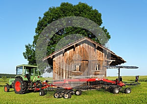 Old Fendt tractor with trailed rotary tedder. Hay ready to be harvested. Wood storage in the countryside for tools