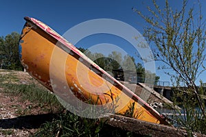 Old fibreglass yellow boat, possibly canoe, drawn ashore in river dam yacht club and tied with chain.