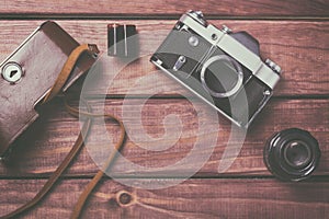 Old film camera with lens, case and film on wooden background. Vintage toned and top view