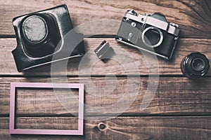Old film camera with lens, case, photo frame and film on wooden background. Vintage toned and top view